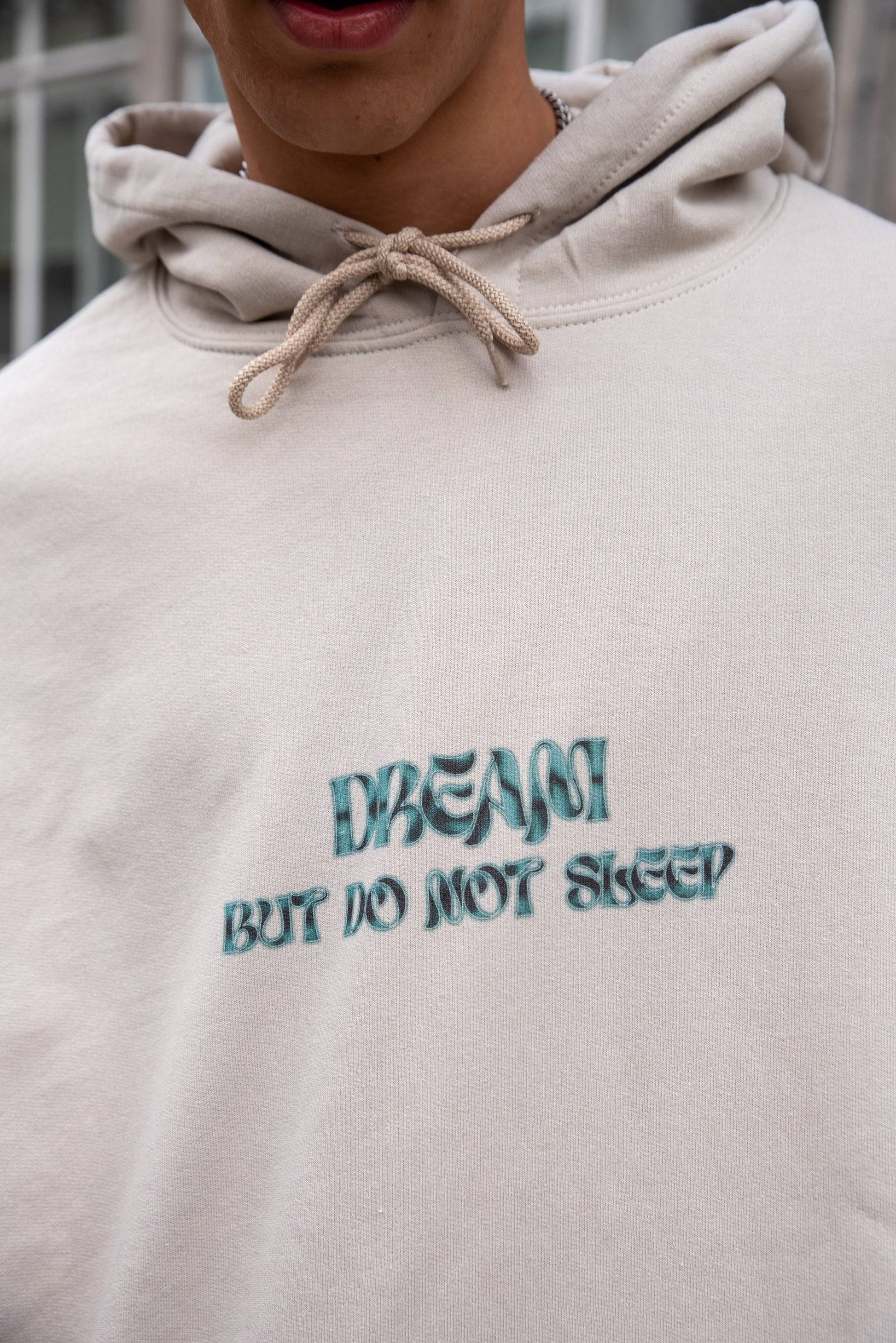 Detailed view of the cursive logo print on the sand-colored unisex hoodie, made from heavyweight cotton for a premium streetwear look.