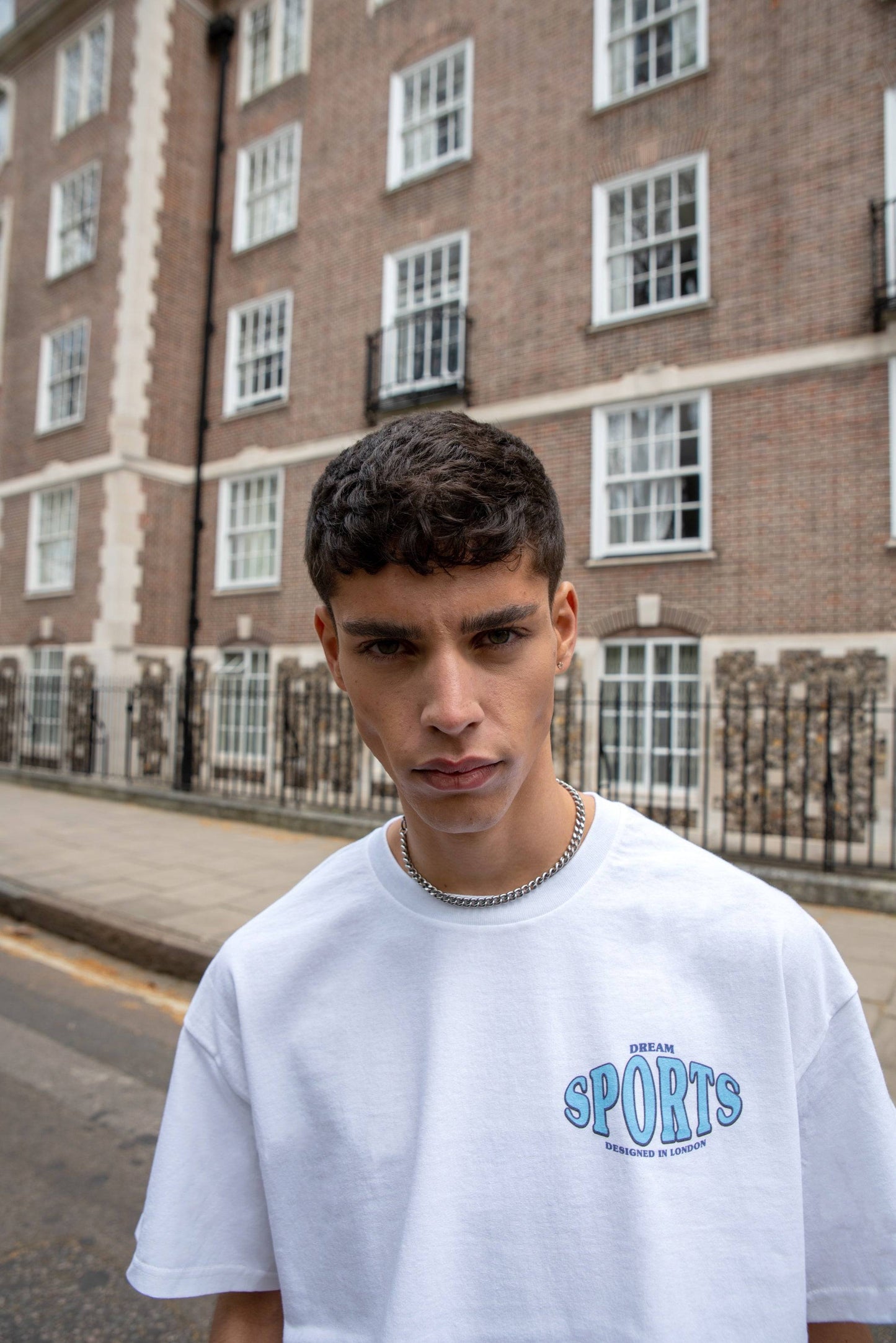 Close-up front view of white sport print t-shirt with dream chest logo, styled with silver chain for a hip hop streetwear look.