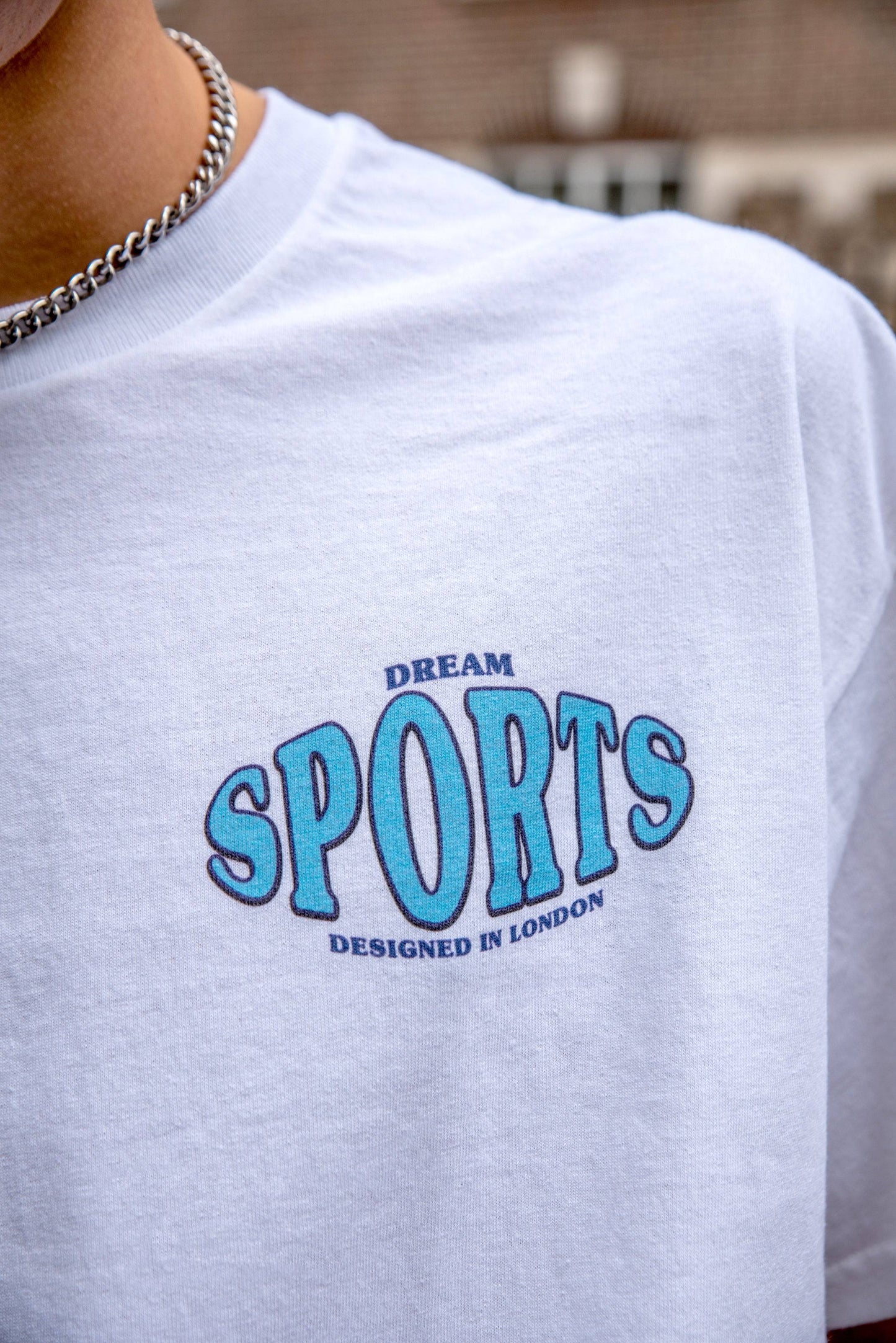 Detailed view of 'Dream Sports Designed in London' chest print on white t-shirt, highlighting graphic design and casual streetwear appeal.