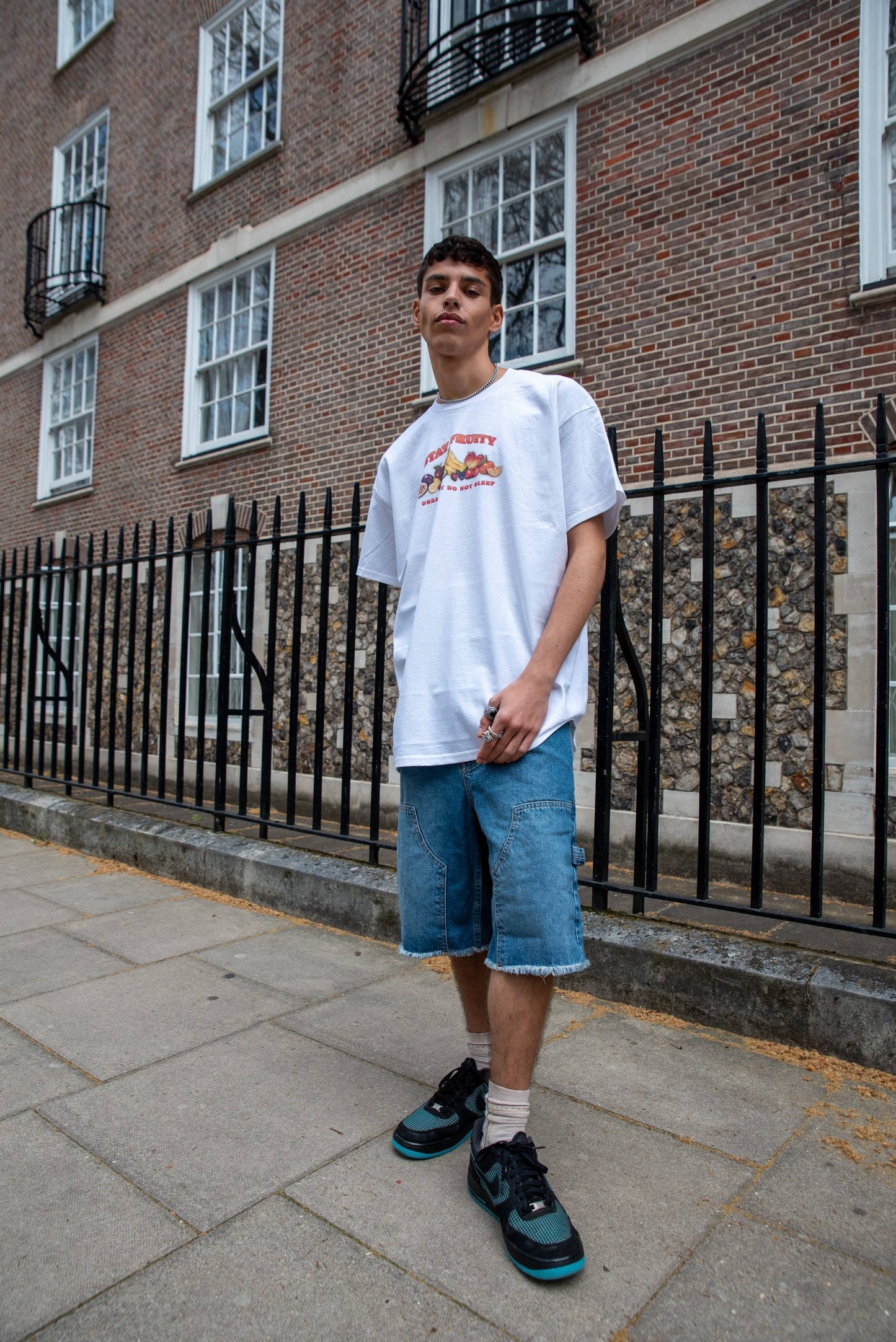 Model wearing White Short Sleeve T-shirt - Stay Fruity Print paired with baggy denim shorts and sneakers, showcasing relaxed streetwear fit.