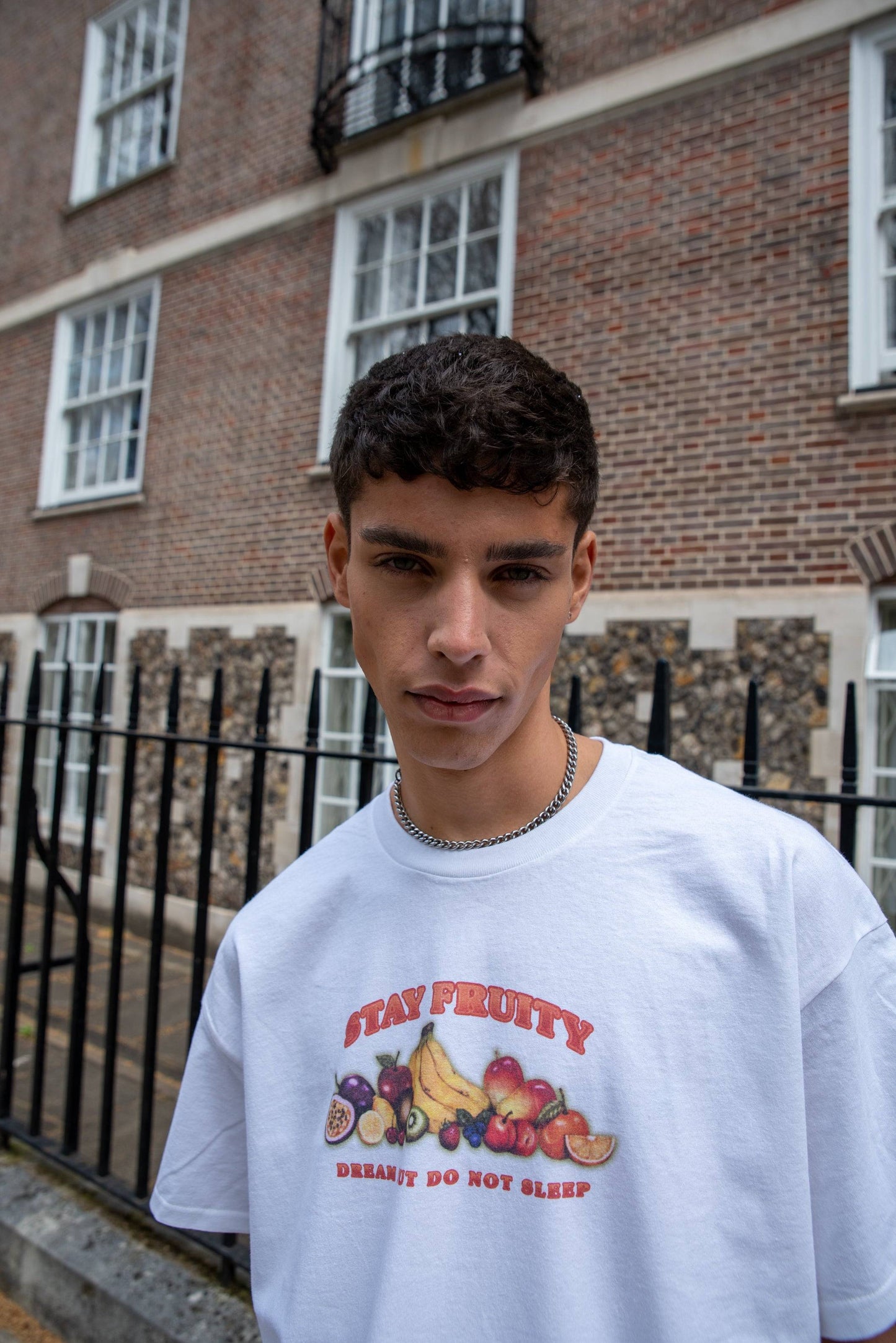Close-up of White Short Sleeve T-shirt - Stay Fruity Print with bold fruit graphic and 'Dream It Do Not Sleep' slogan, worn in casual street style.