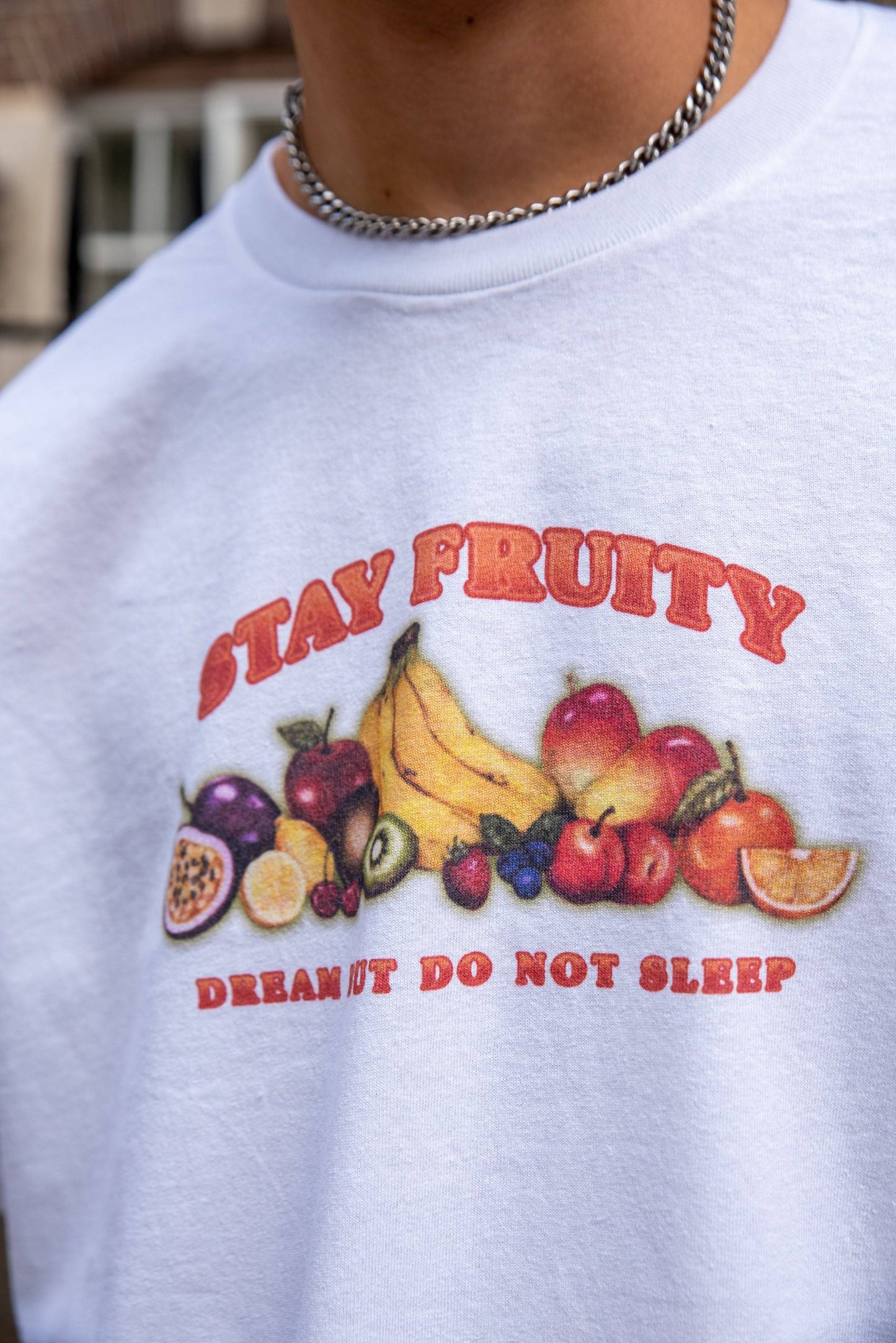 Detailed view of Stay Fruity Print on white short sleeve T-shirt showing vibrant fruit illustration and motivational slogan in red text.