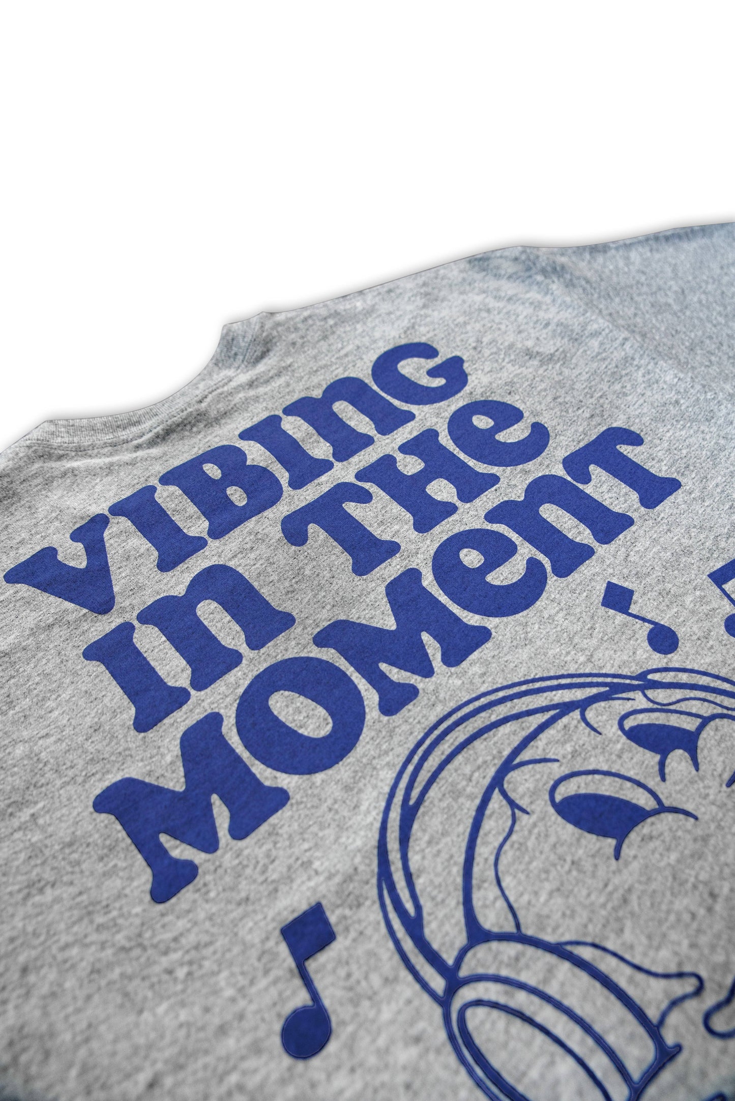 Angled view of grey t-shirt showing 'Vibing in the Moment' slogan and music notes in blue print. Stylish and breathable cotton tee.