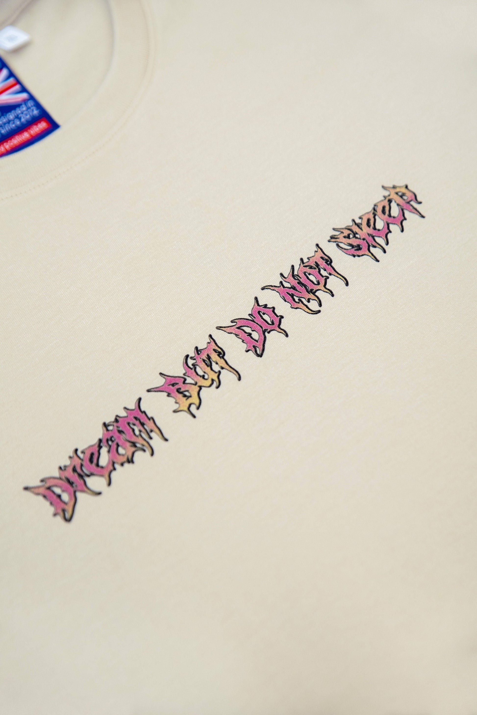 Close-up of chest text 'Dream Next Do Not Sleep' on sand t-shirt, featuring sharp graphic typography for a unique streetwear look.