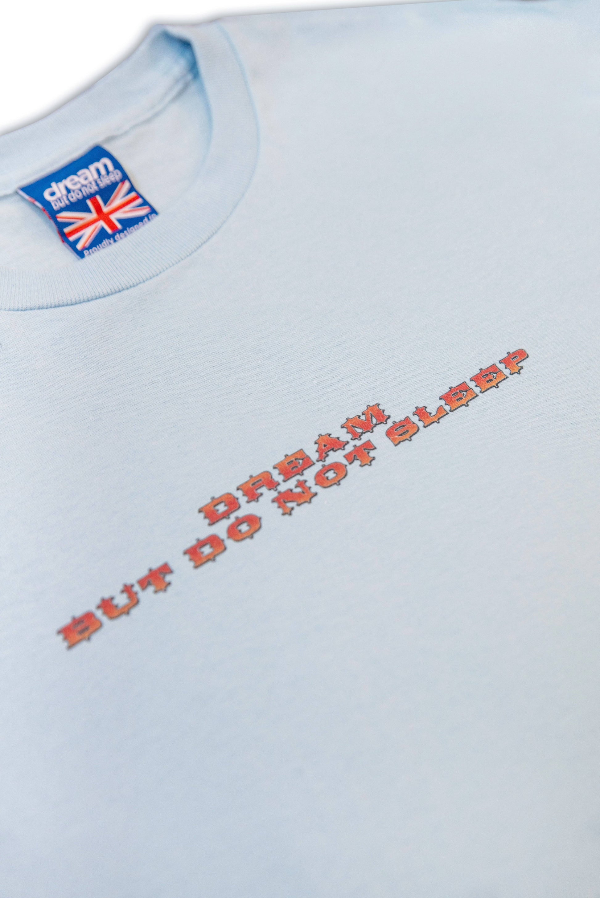 Close-up of chest text 'Dream But Do Not Sleep' on blue short sleeved t-shirt, printed in bold red pixelated font.