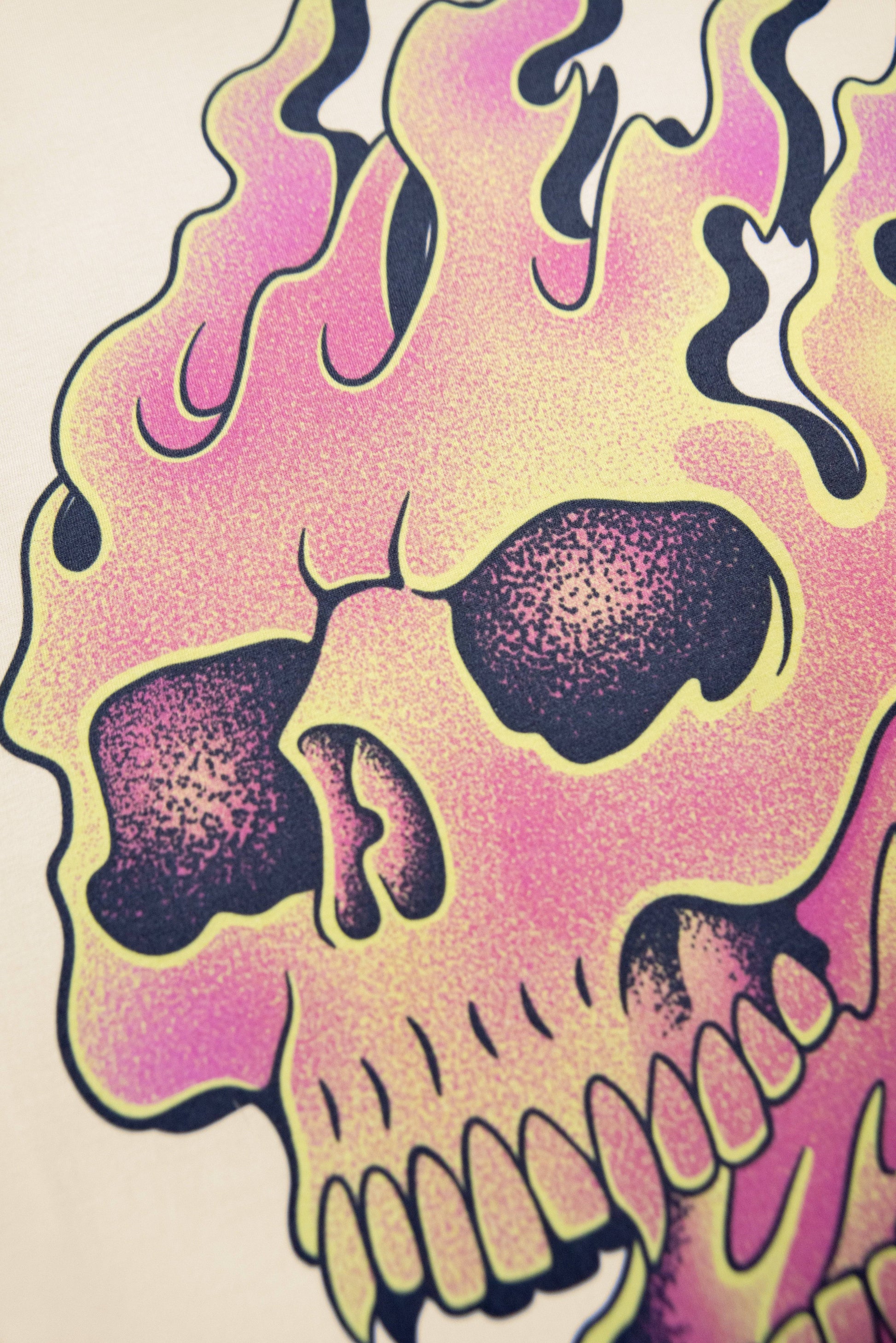 Close-up of flaming skull print on sand short sleeved t-shirt, showcasing vivid pink and yellow fire details for edgy fashion appeal.
